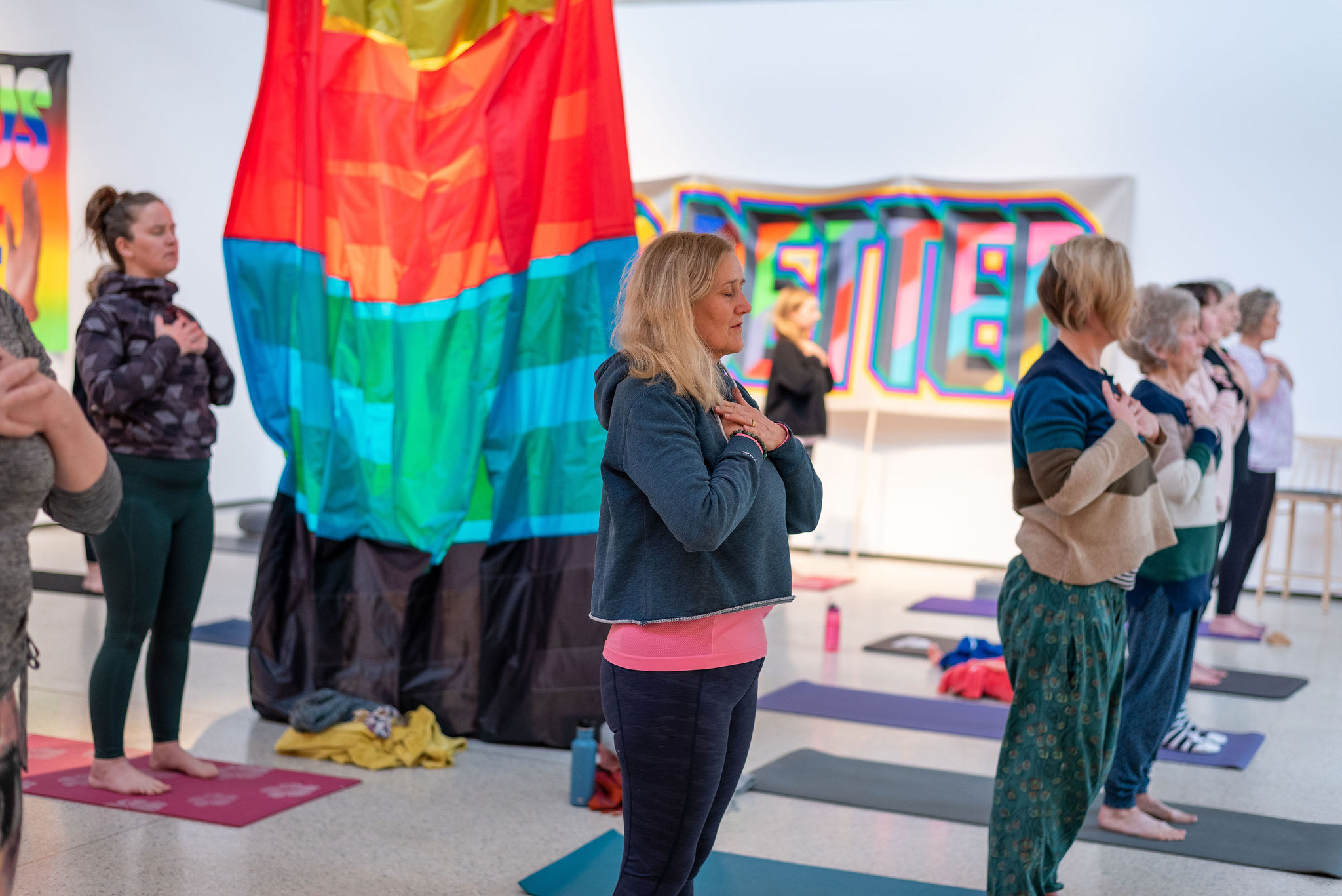 A group of people practicing yoga inside a gallery space, with colourful fabric hangings and paintings.