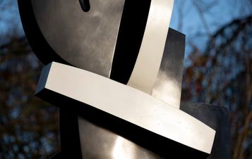 Close up of a black and white abstract sculpture displayed on plinths outdoors, with trees behind it.