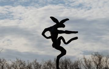 A sculpture of a hare balanced on the tip of an oversized anvil, displayed outdoors.