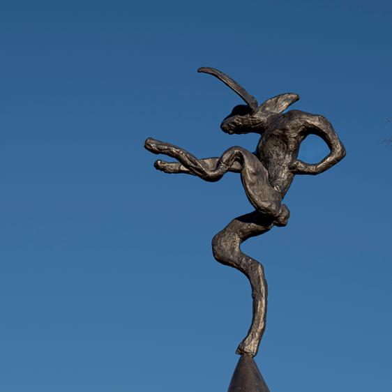 A sculpture of a hare balanced on the tip of an oversized anvil, displayed outdoors.
