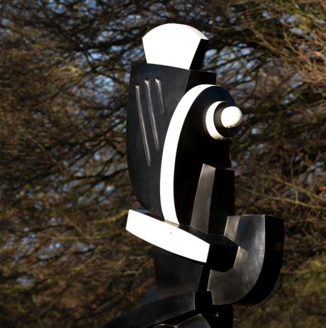 Close up of a black and white abstract sculpture displayed on plinths outdoors, with trees behind it.