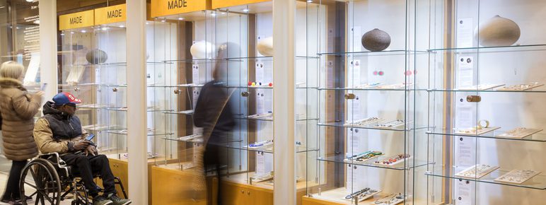 A group of people, including a wheelchair user, looking at jewellery and ceramics in glass fronted display cases.