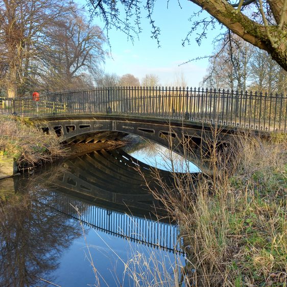A cast iron bridge spanning a waterway, surrounded by trees
