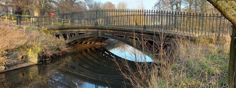 A cast iron bridge spanning a waterway, surrounded by trees