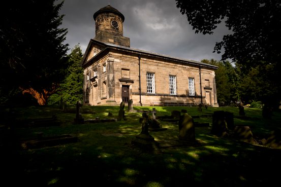 A large chapel surrounded by trees and a graveyard.