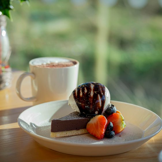 A plate of cheesecake, ice cream and strawberries, and a cup of frothy coffee on a table