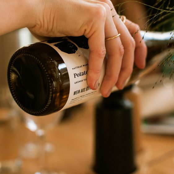 A close up of a hand pouring a bottle of wine into a glass
