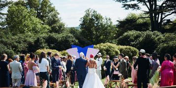 A bride and escort, walking down an outdoor aisle surrounded by their guests.