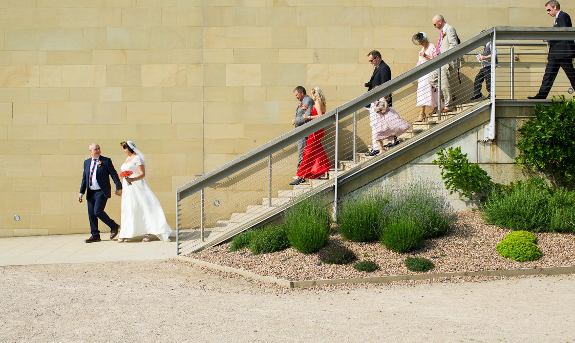 A wedding part, led by the bride and groom, walking down steps outside the Underground Gallery at YSP
