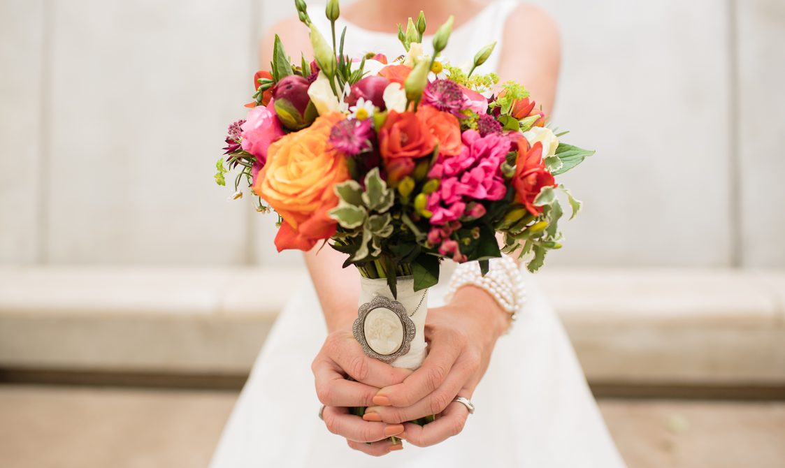 A bride holding a bouquet of orange and pink flowers.