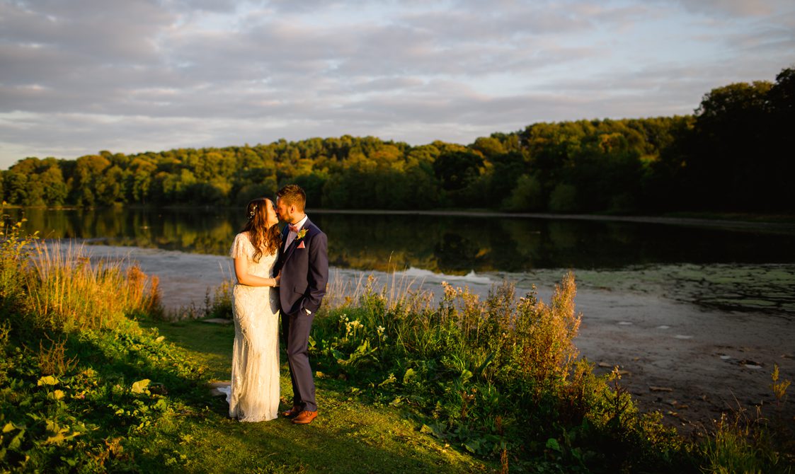 A bride and groom standing in front of a lake