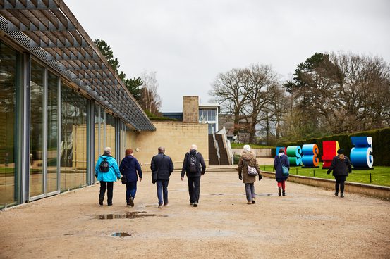 A group of walkers in winter coats walking outside a glass wall outside the Underground Gallery.
