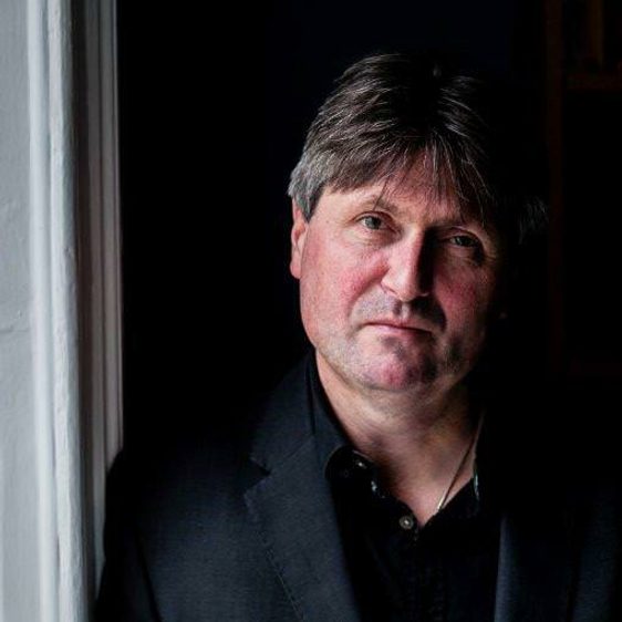 A white man with brown hair, wearing a black suit