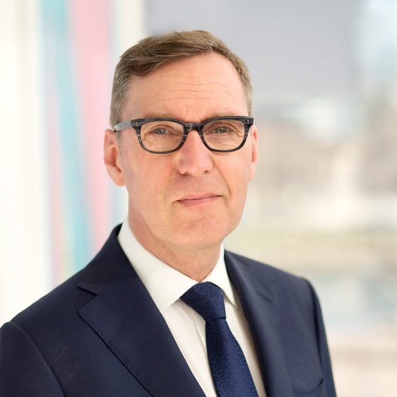 A white man with brown hair wearing glasses and a blue suit and tie.