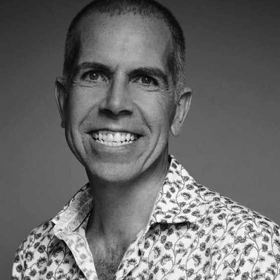 A headshot of a man wearing a patterned white shirt