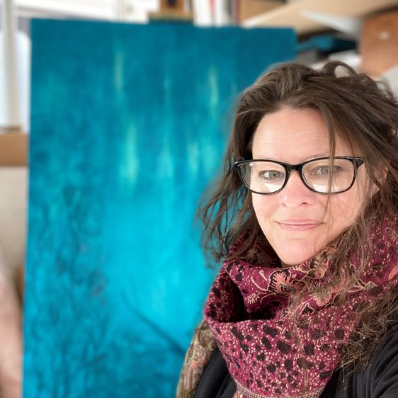 A woman with long brown hair and black glasses, wearing a scarf.