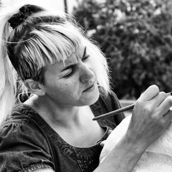 A black and white photo of a woman with a fringe painting a clay figure