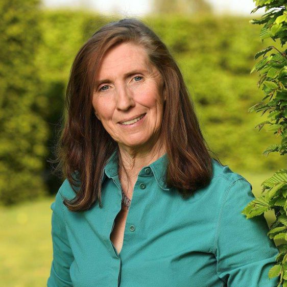 A white woman with brown hair shoulder length hair, wearing a green shirt