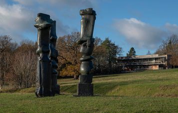 Three tall thin bronze sculptures with YSP Centre behind them