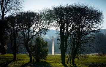 A tall pointed tower, with glass panels, seen between trees.