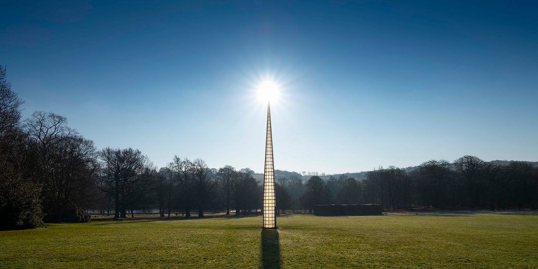 A tall pointed tower, with glass panels. The sun is rising behind it.