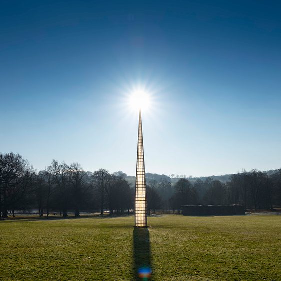 A tall pointed tower, with glass panels. The sun is rising behind it.