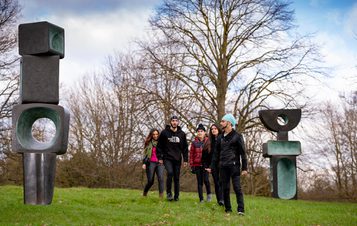 A group of people standing in front of Barbara Hepworth, The Family of Man at Yorkshire Sculpture Park