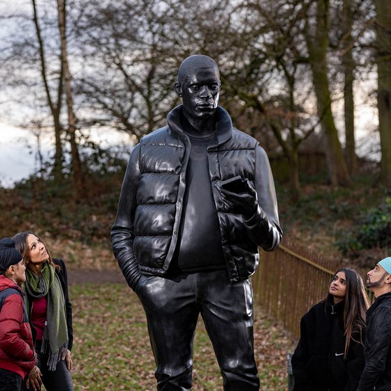 Four people looking up at a larger-than-life-size sculpture of a man holding a mobile phone.