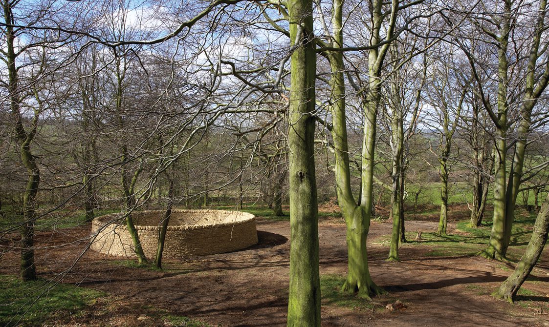 A circular dry stone wall in woodland.