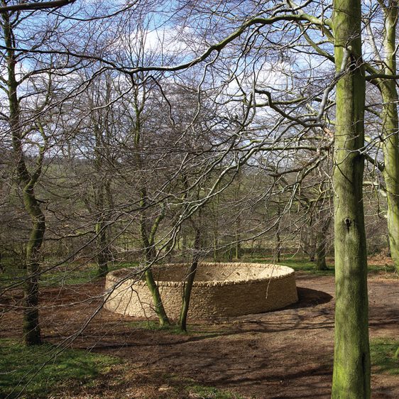 A circular dry stone wall in woodland.