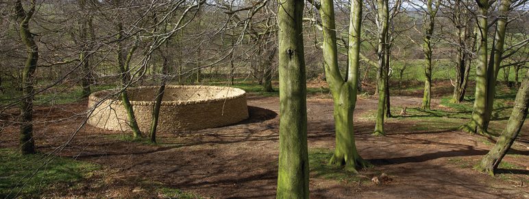 A circular dry stone wall in woodland.