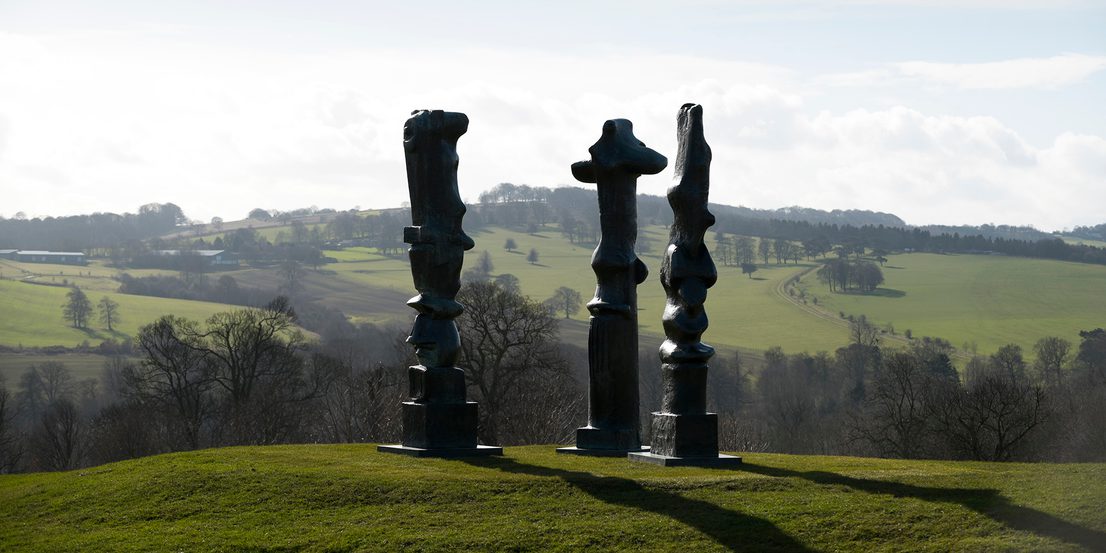 Three tall thin bronze sculptures looking out over the landscape
