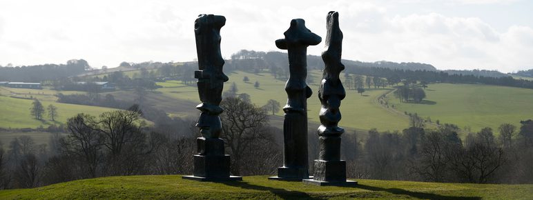 Three tall thin bronze sculptures looking out over the landscape