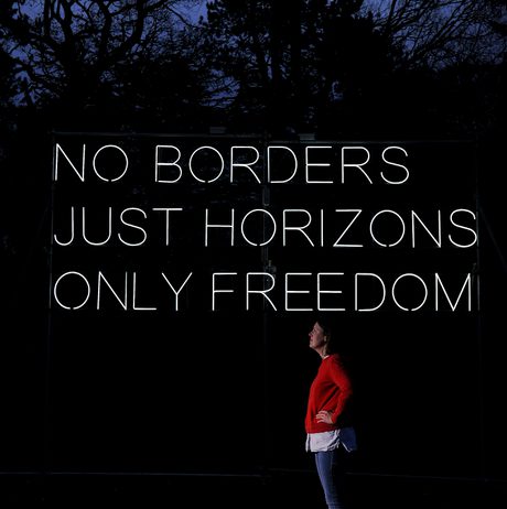 A white woman standing in front of Hilary Jack No Borders 2018 lit up at Yorkshire Sculpture Park