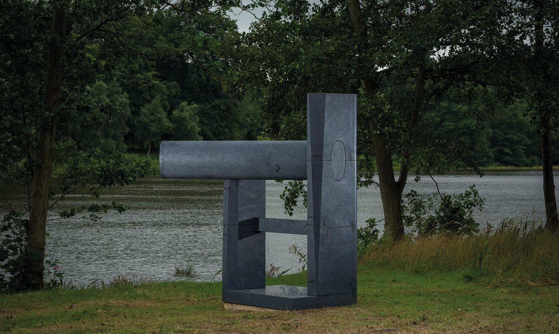 A dark grey abstract sculpture next to a lake