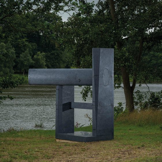 A dark grey abstract sculpture next to a lake