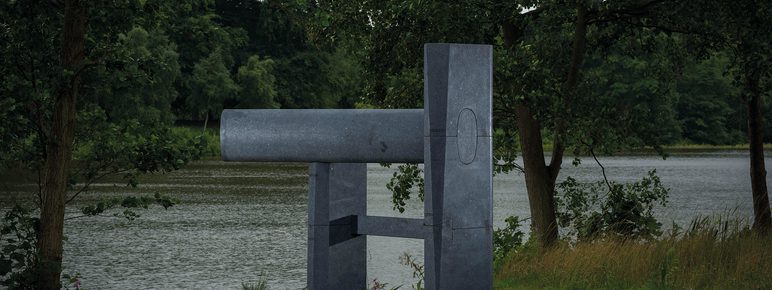 A dark grey abstract sculpture next to a lake
