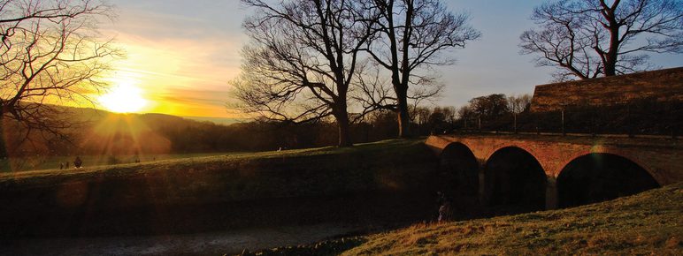 The sun rising over a brick deer shelter, surrounded by trees.