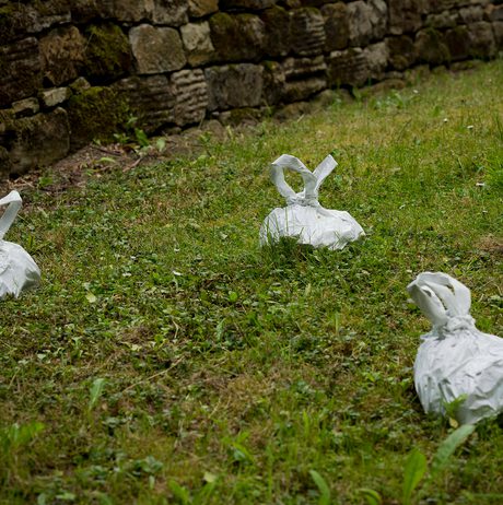 A group of white sculptures in the shape of dog-poo bags, on grass