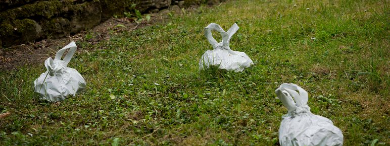 A group of white sculptures in the shape of dog-poo bags, on grass