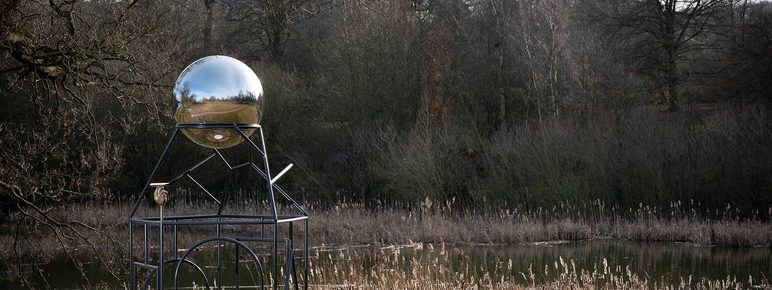 A metal frame sculpture with a silver ball at the top.