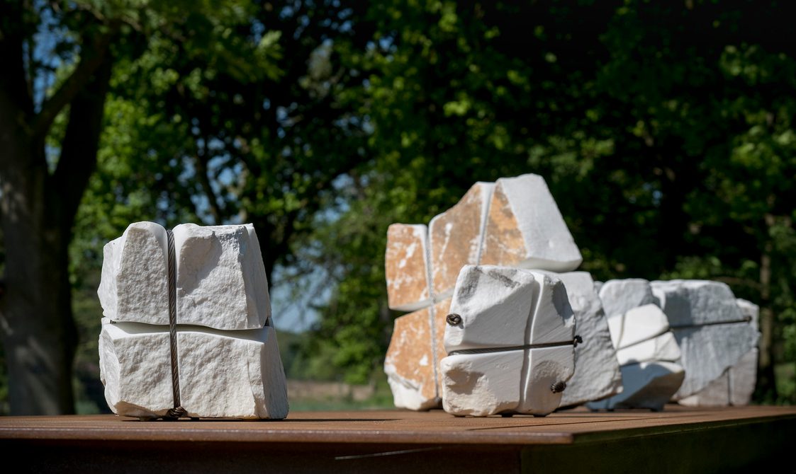 A bronze table structure with white marble pieces wrapped in wire on top.