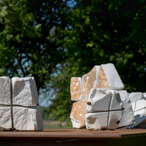 A bronze table structure with white marble pieces wrapped in wire on top.