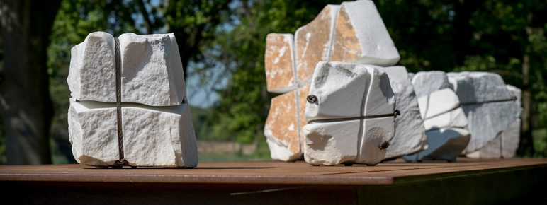 A bronze table structure with white marble pieces wrapped in wire on top.