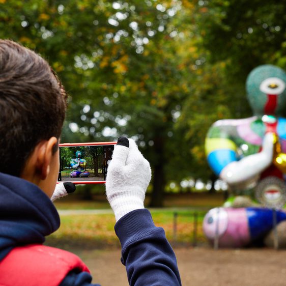 A boy taking a phone photograph of a brightly coloured mosaic Buddha figure.