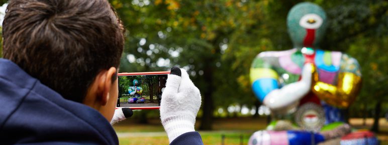A boy taking a phone photograph of a brightly coloured mosaic Buddha figure.