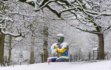 A seated humanoid figure covered in brightly coloured mosaic tiles in the snow