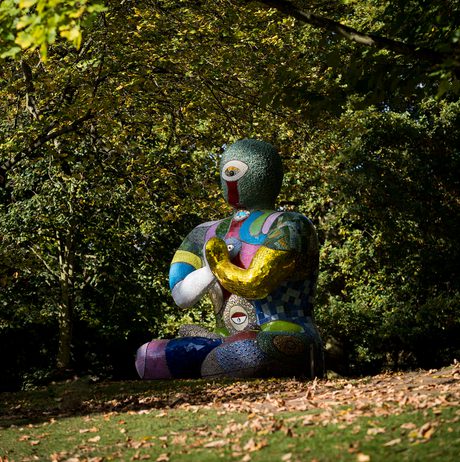 A seated humanoid figure covered in brightly coloured mosaic tiles