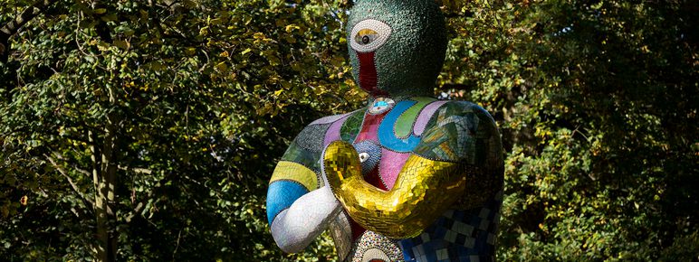 A seated humanoid figure covered in brightly coloured mosaic tiles