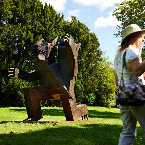 A group of people standing near to a 2 headed bear sculpture outdoors